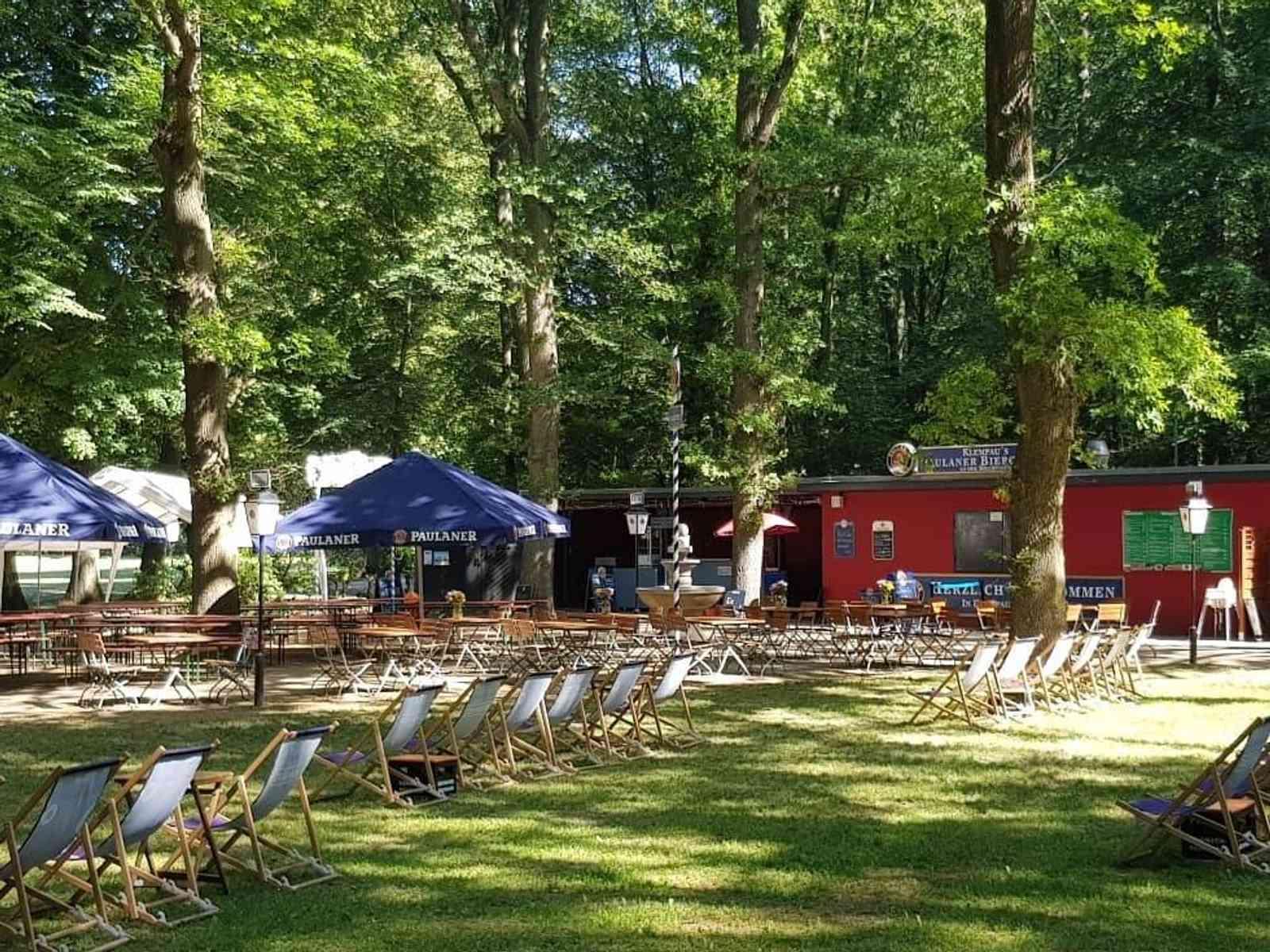 Biergarten mit Bierzeltgarnituren und Sonnenschirmen im Grünen