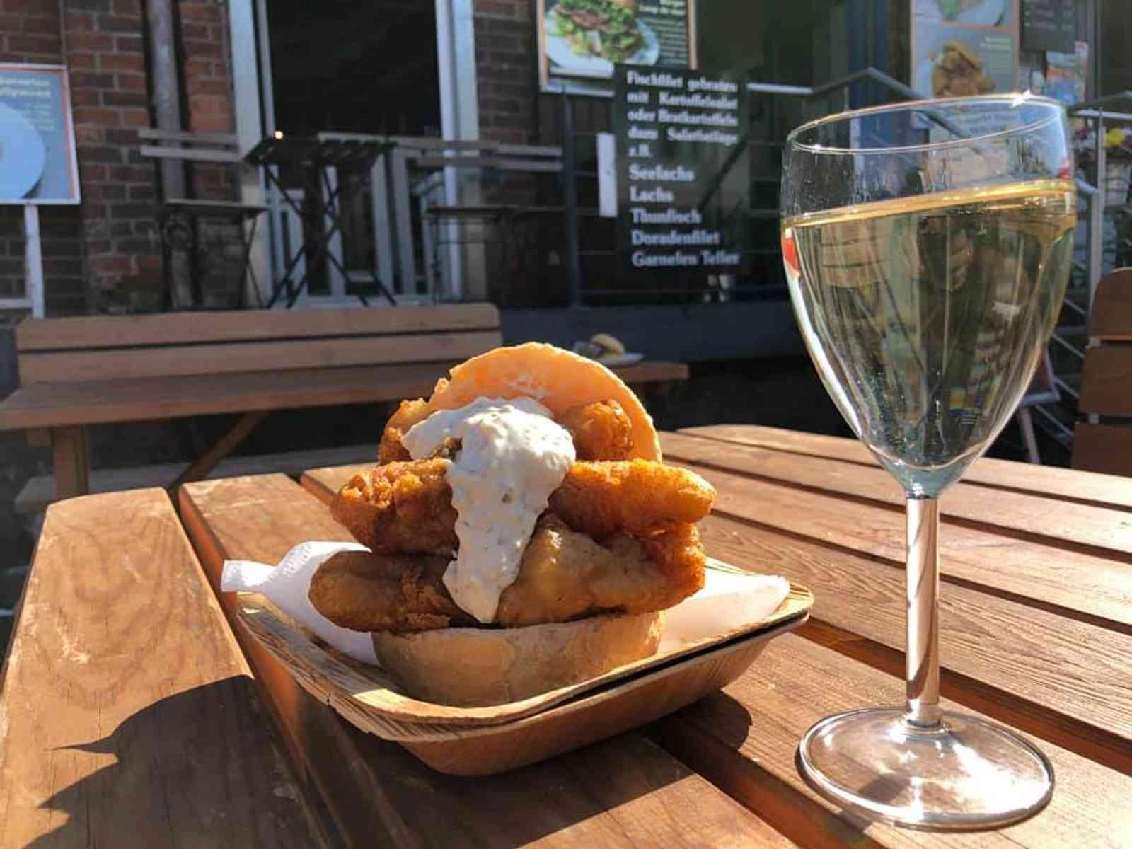 Backfischbrötchen mit Remoulade neben einem Glas Weißwein