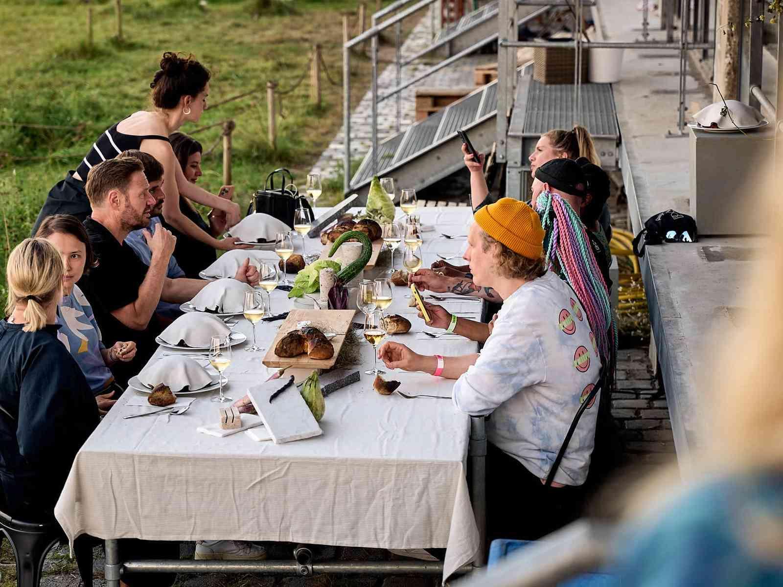 Personen sitzen an einem Tisch mit weißer Tischdecke und trinken Wein