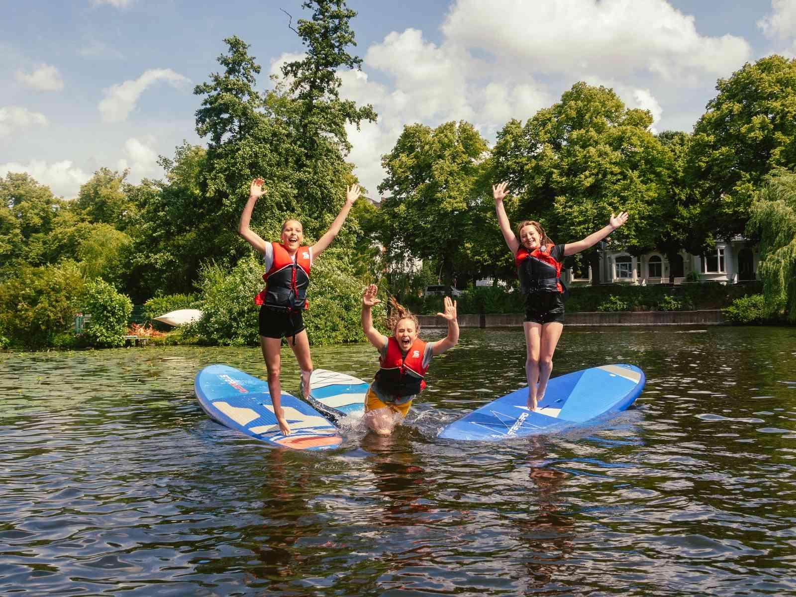 Drei junge Frauen springen von SUPs ins Wasser und lachen in die Kamera