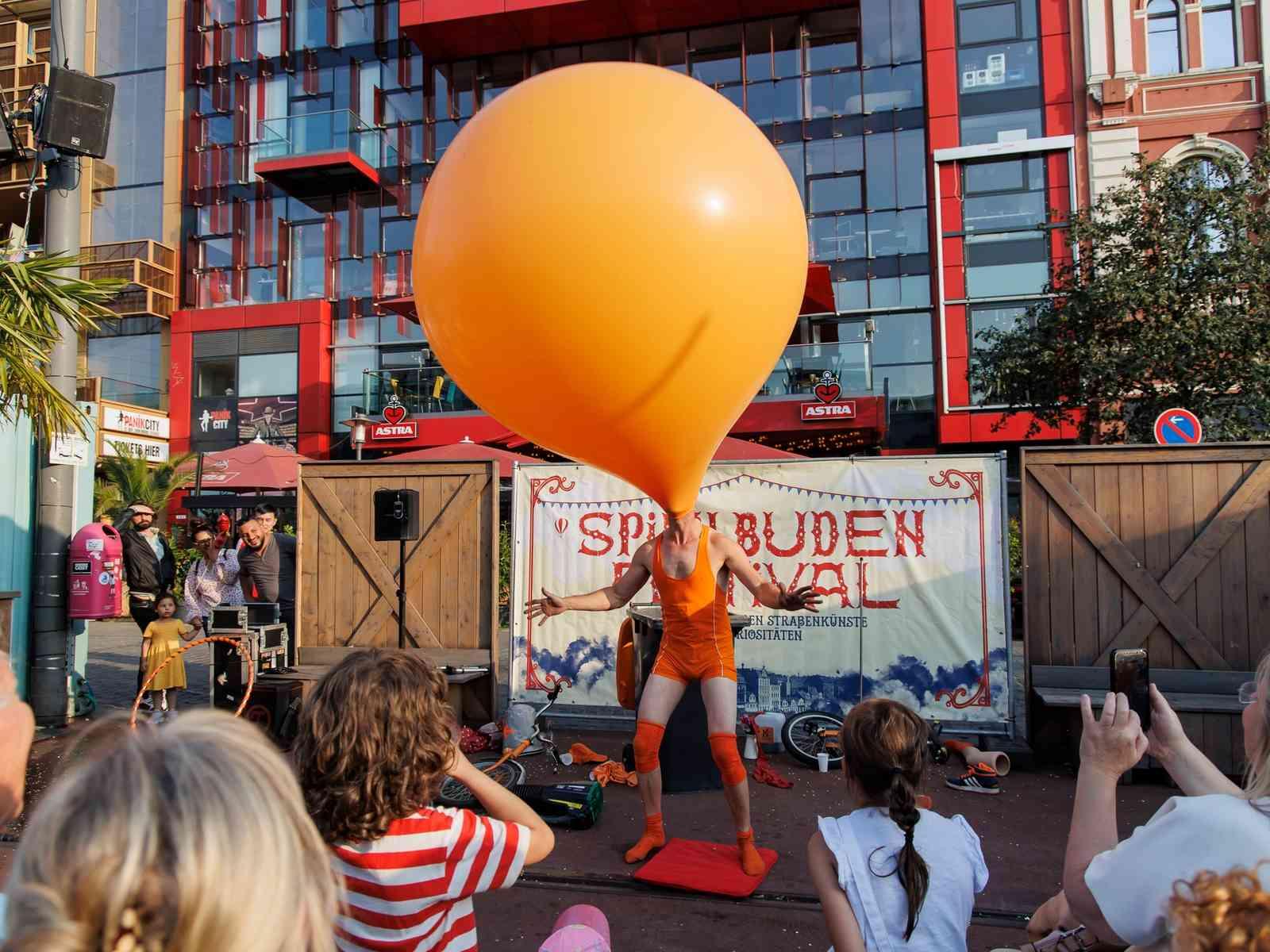 Kleinkünstler steht mit Ballon auf dem Kopf vor Publikum