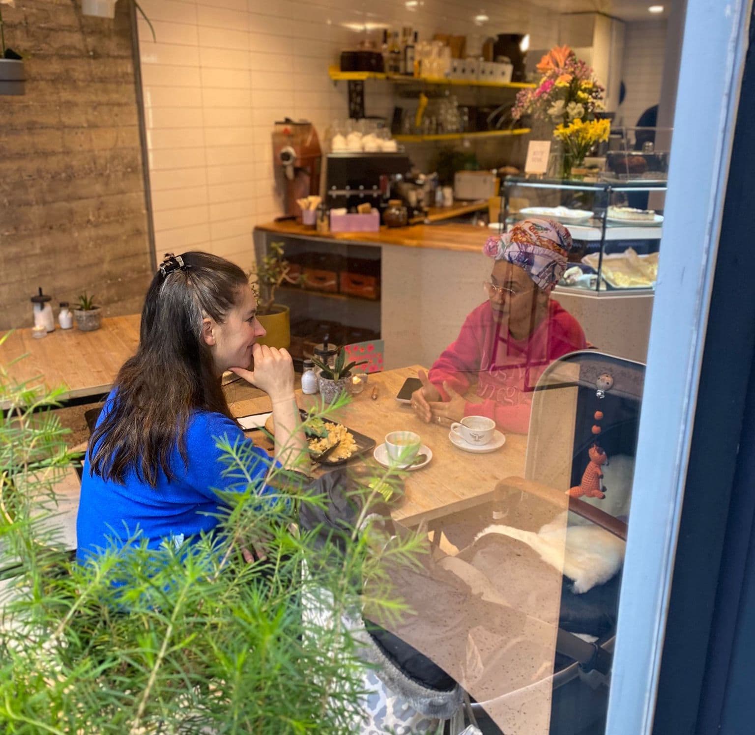 Zwei Frauen sitzen mit einem Kinderwagen im Café am Tisch