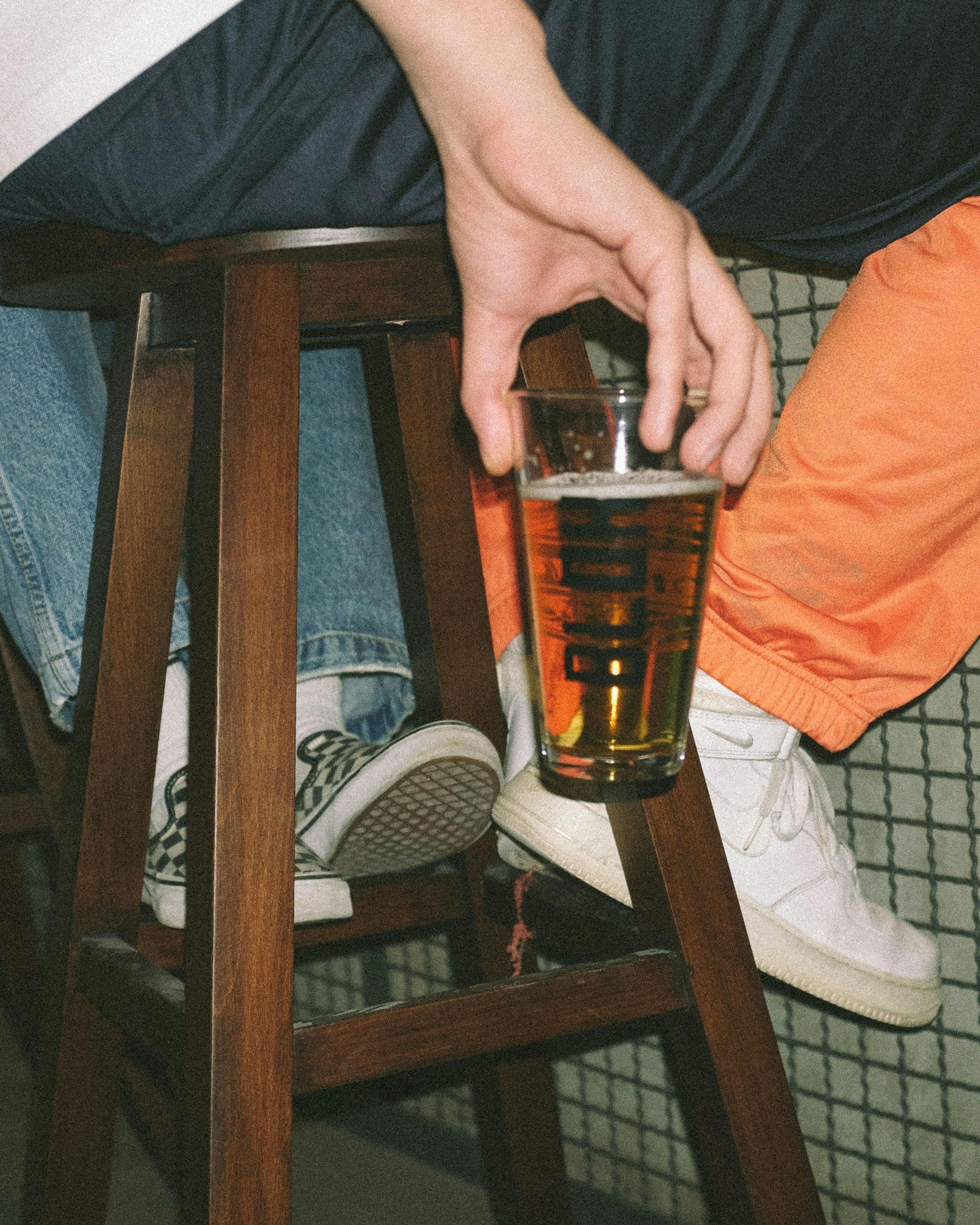 Eine Person sitzt auf einem Hocker und hält ein gefülltes Glas in der Hand