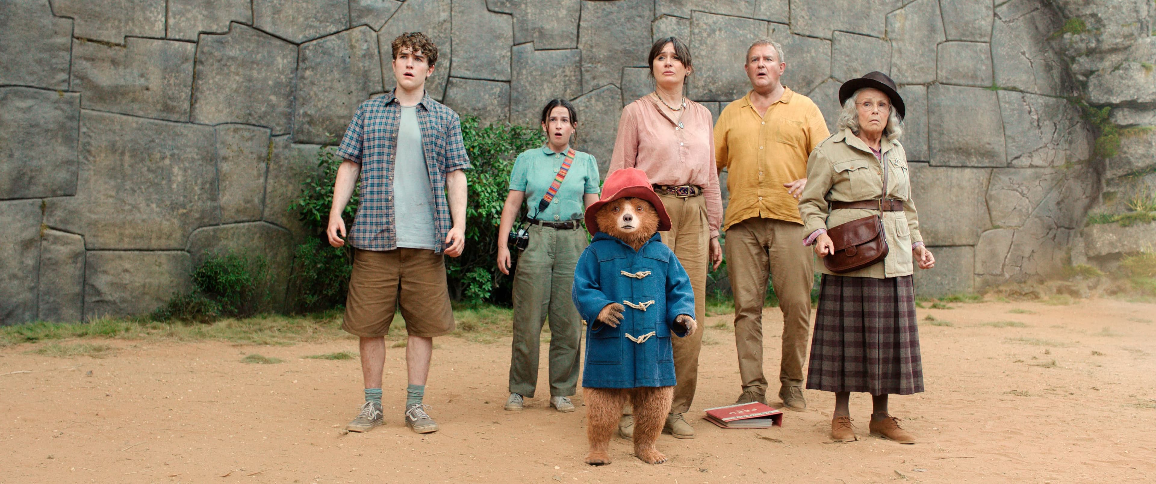 Paddington, Mrs Bird und die Familie Brown stehen vor einer Steinwand.