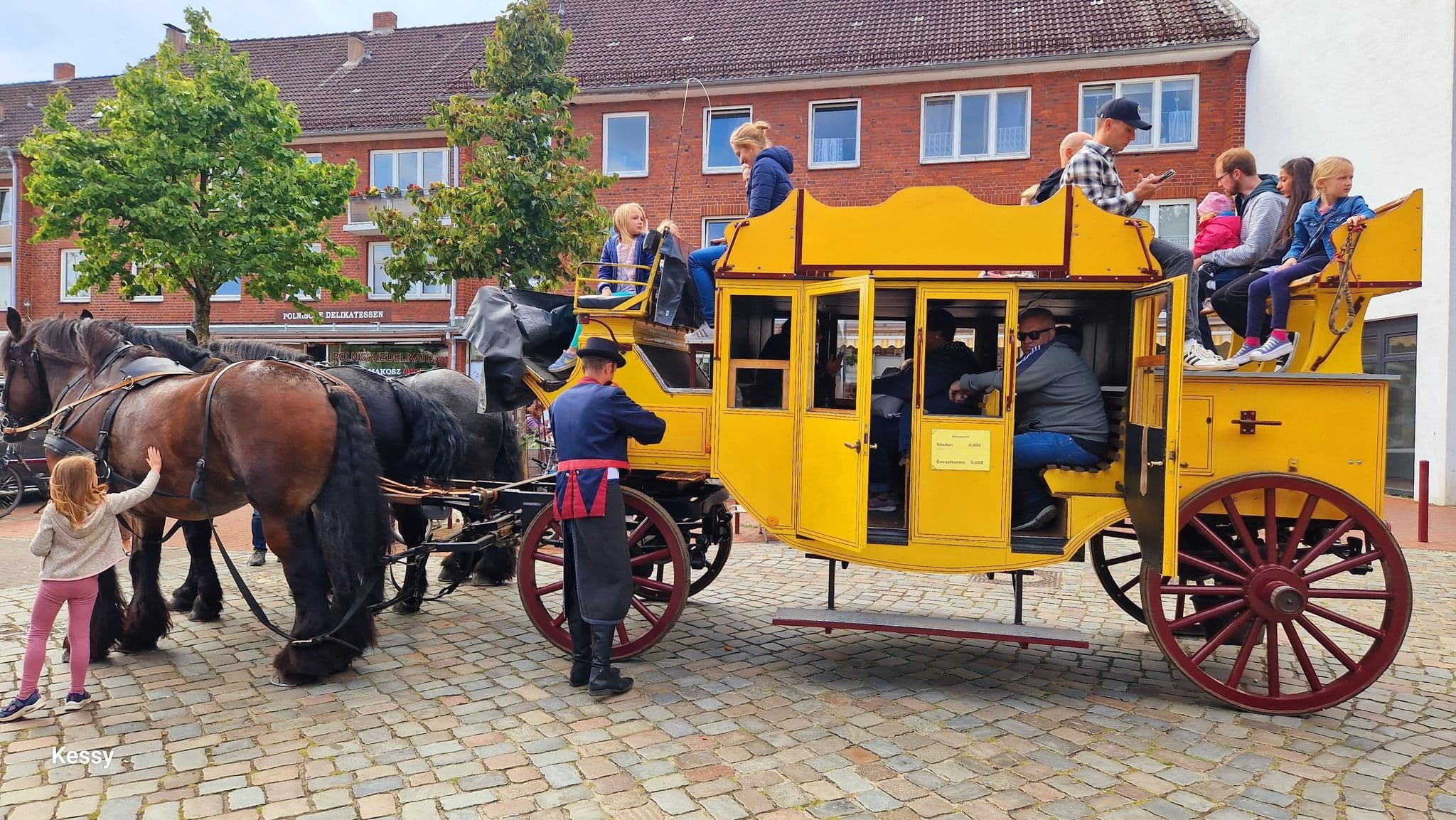Auf einer gelben Postkutsche sitzen Menschen