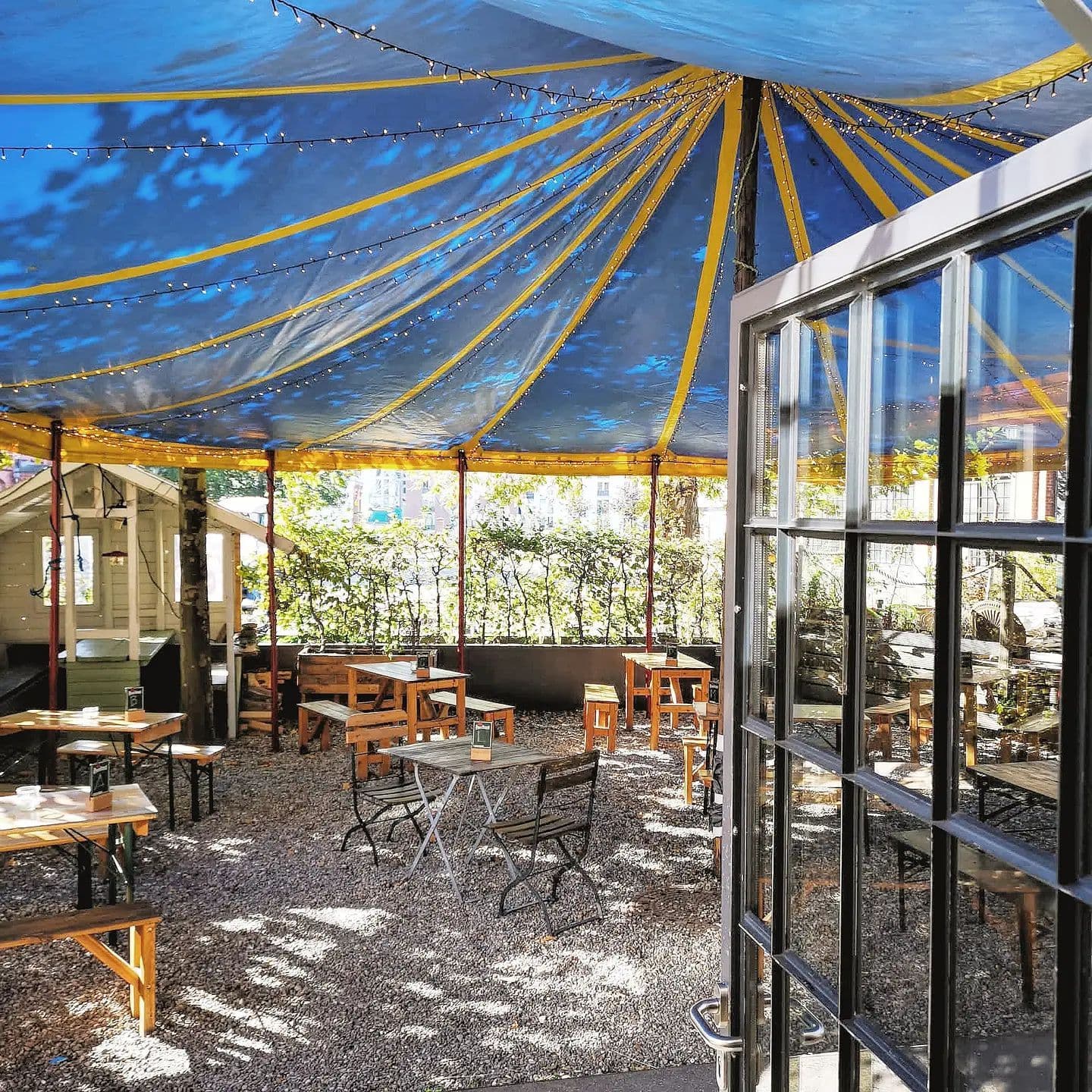 Tische und Stühle stehen in einem Zirkuszelt auf einem Innenhof