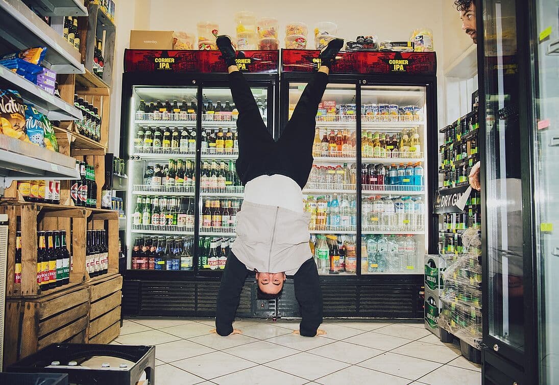 Foto eines Mannes im Handstand, der sich im Supermarkt/Kiosk befindet