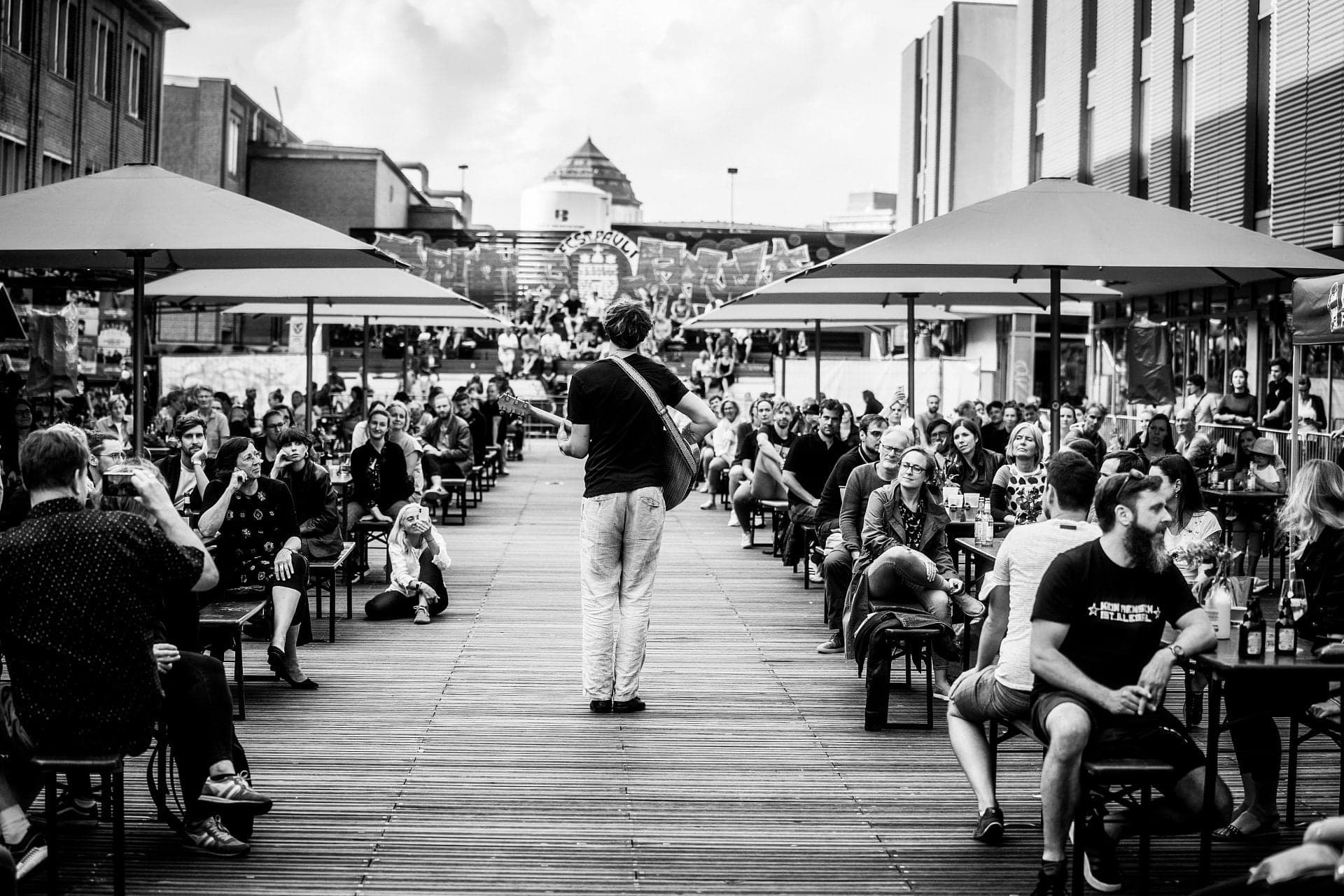Person geht mit einer Gitarre zwischen Menschen auf dem Lattenplatz.