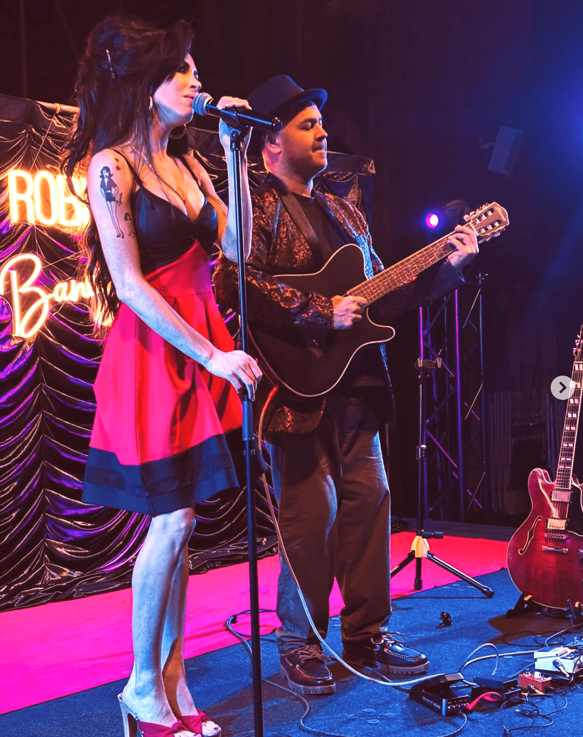 Robin Banerjee und eine Frau, die aussieht wie Amy Winehouse stehen gemeinsam auf der Bühne