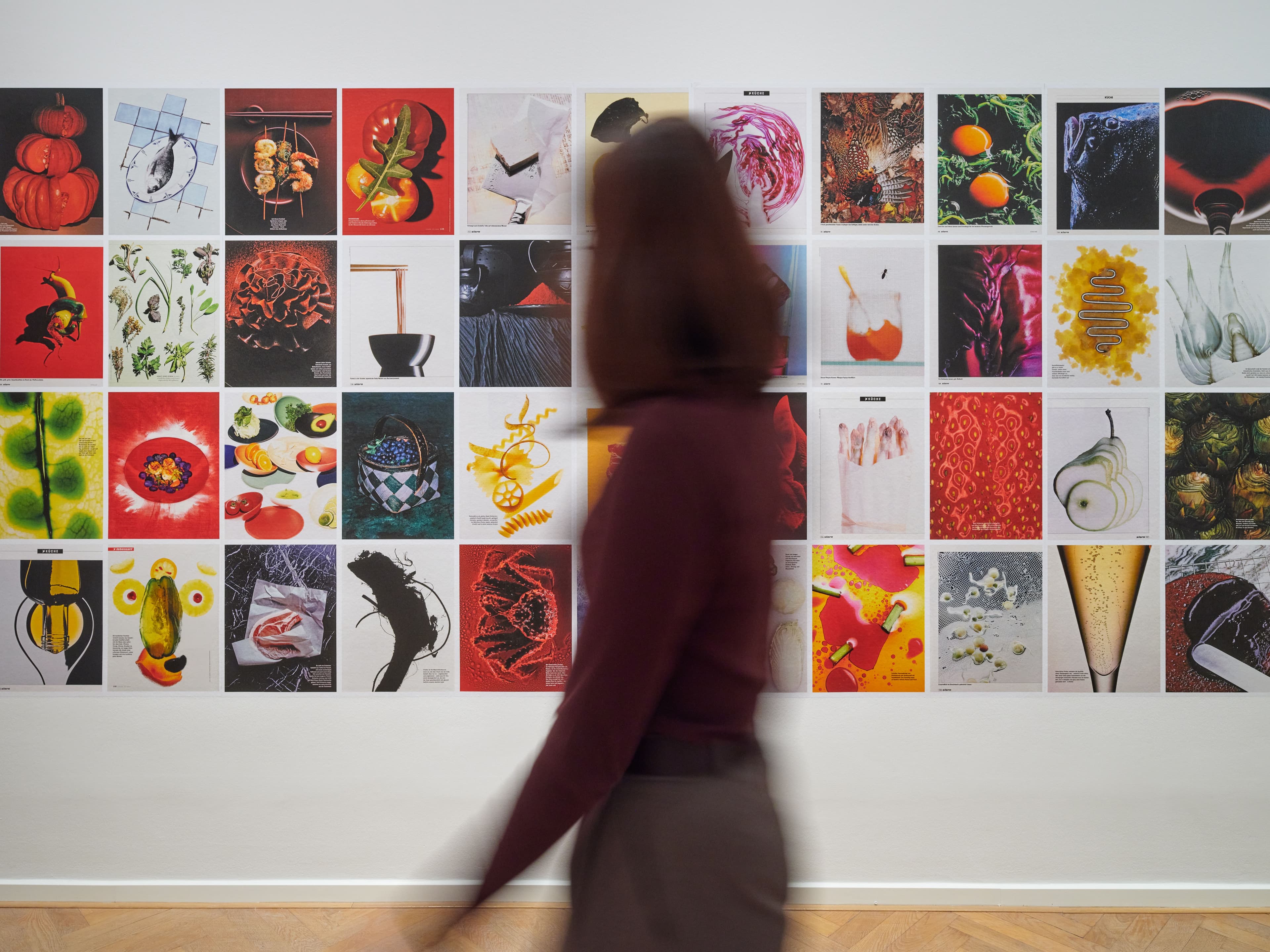 Eine Frau läuft an einer Wand vorbei, an der ganz viele Fotos von Hans Hansen hängen