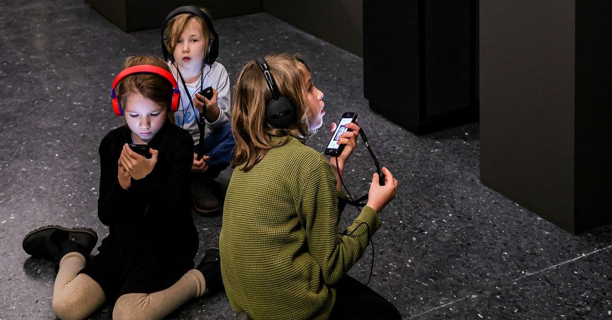 Drei Kinder sitzen mit Kopfhörern auf dem Boden