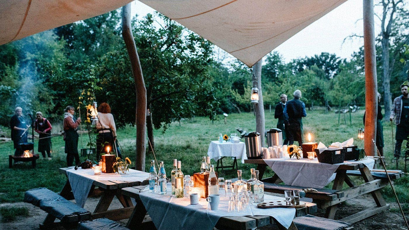 Menschen stehen auf einer Wiese mit gedeckten Tischen