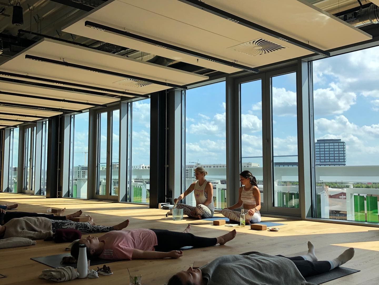 Eine Gruppe an Frauen sitzt und liegt auf Yoga-Matten vor einer großen Fensterfront.