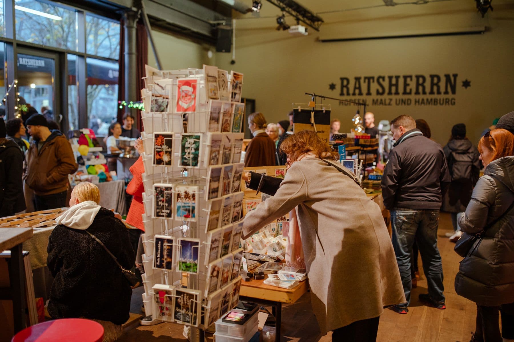 Eine Frau schaut sich einen Stand mit selbstgemachten Postkarten auf dem Schanzenmarkt an