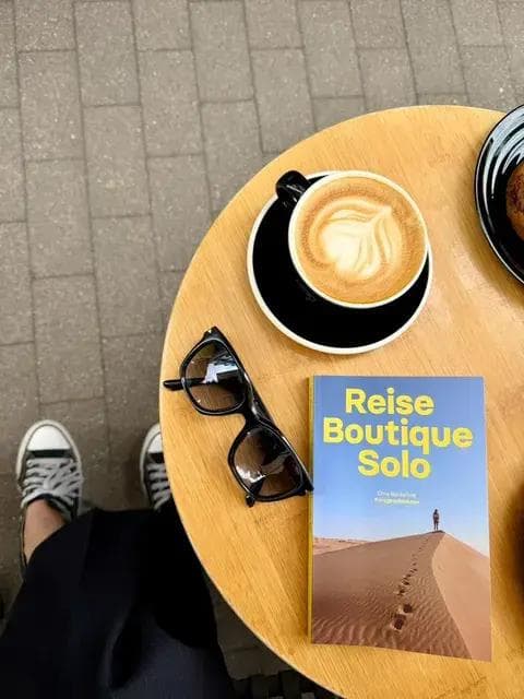 Das Buch "Reise Boutique Solo", eine Tasse Kaffee und eine Sonnenbrille auf einem Tisch