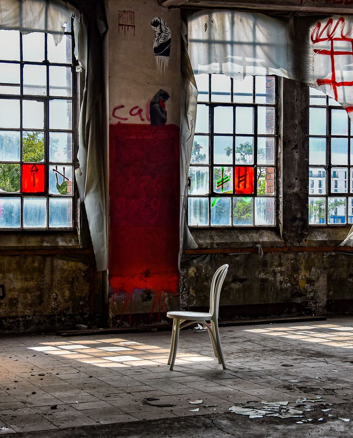 Foto eines Lost Places. Ein Stuhl steht mitten in einer verfallenen Fabrikhalle, in die Sonnenlicht einfällt.