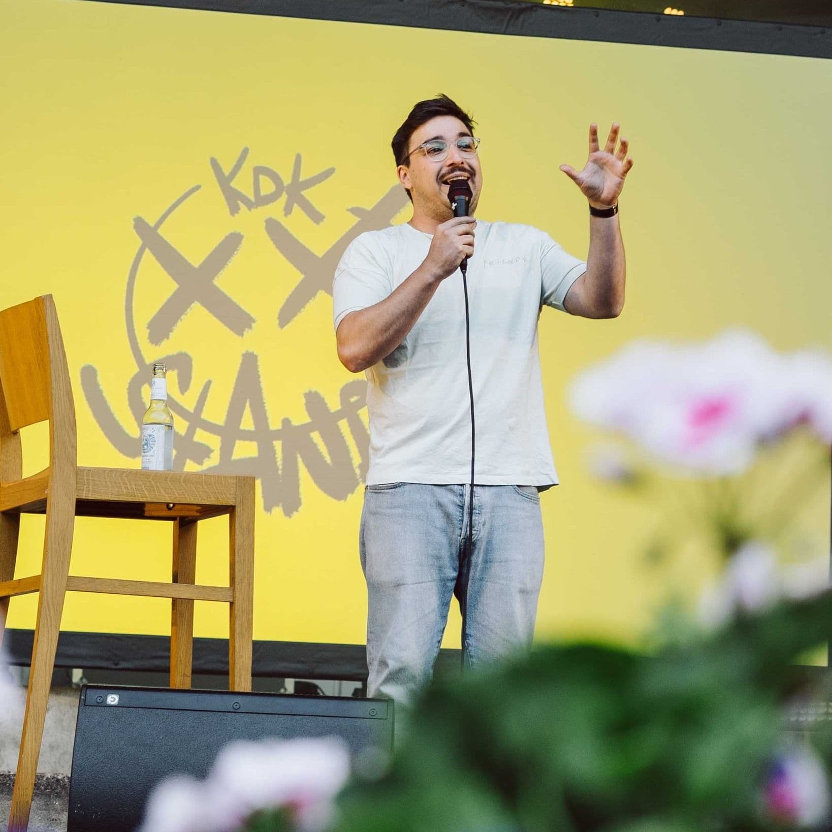 Ein männlicher Comedian bei einem KdK-Stand up steht mit einem Mikrofon auf der Bühne