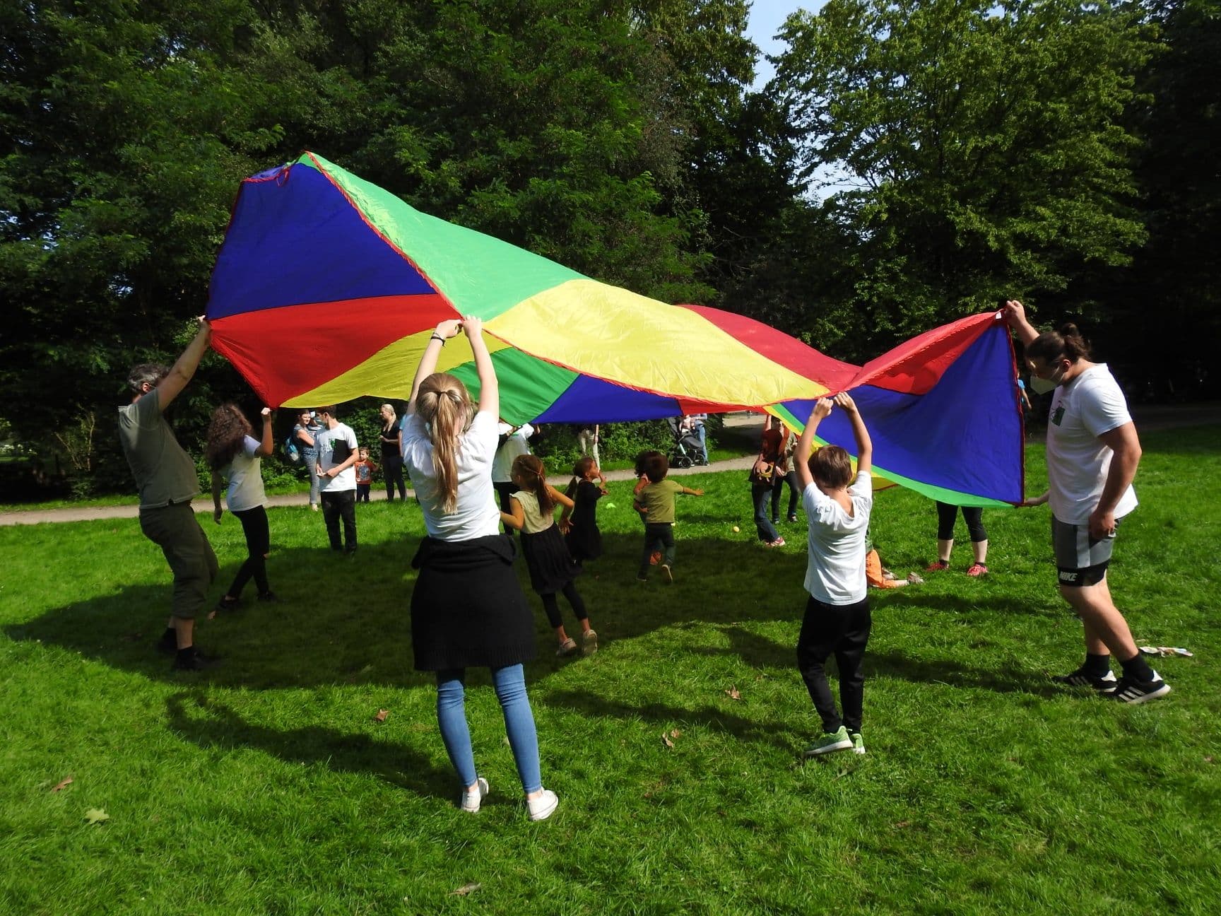 Kinder schwingen ein großes buntes Tuch, gemeinsam in die Luft.