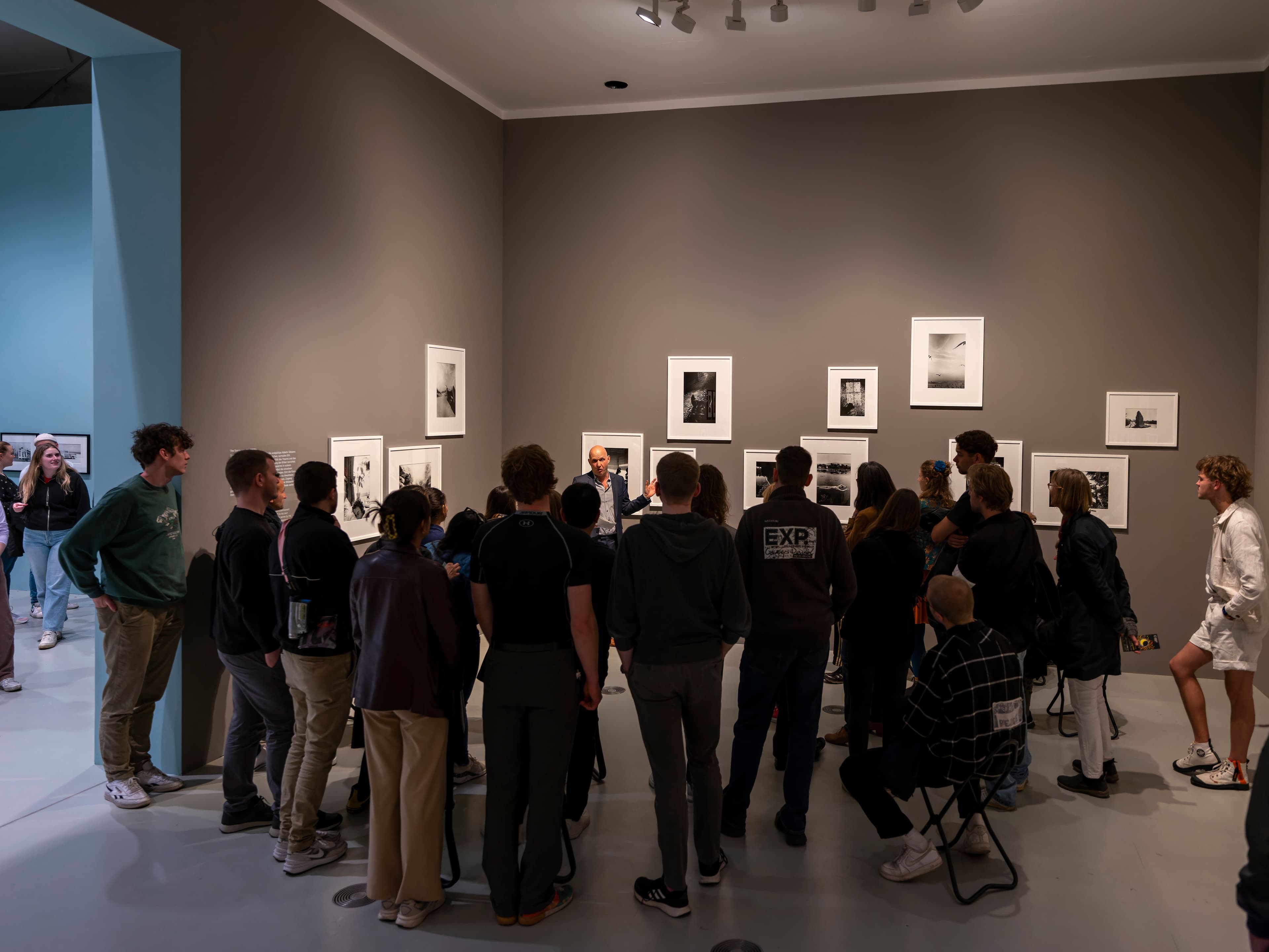 Eine Gruppe Menschen steht in einem Museum vor einer Wand mit Bildern
