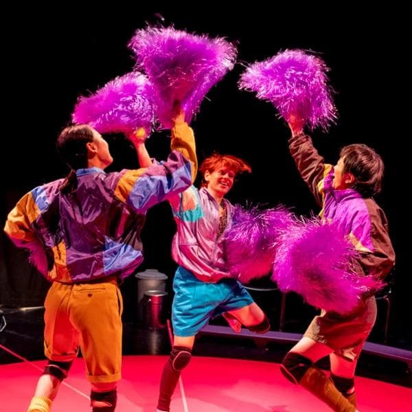 Drei tanzende Performer:innen in bunten Kostümen