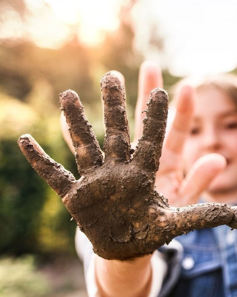 Eine Kinderhand voller Dreck und Erde