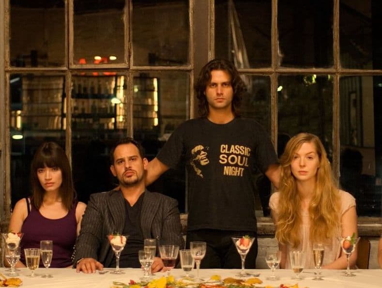 Schauspieler:innen aus dem Film Soul Kitchen stehen an einer gedeckten Tafel und schauen in die Kamera
