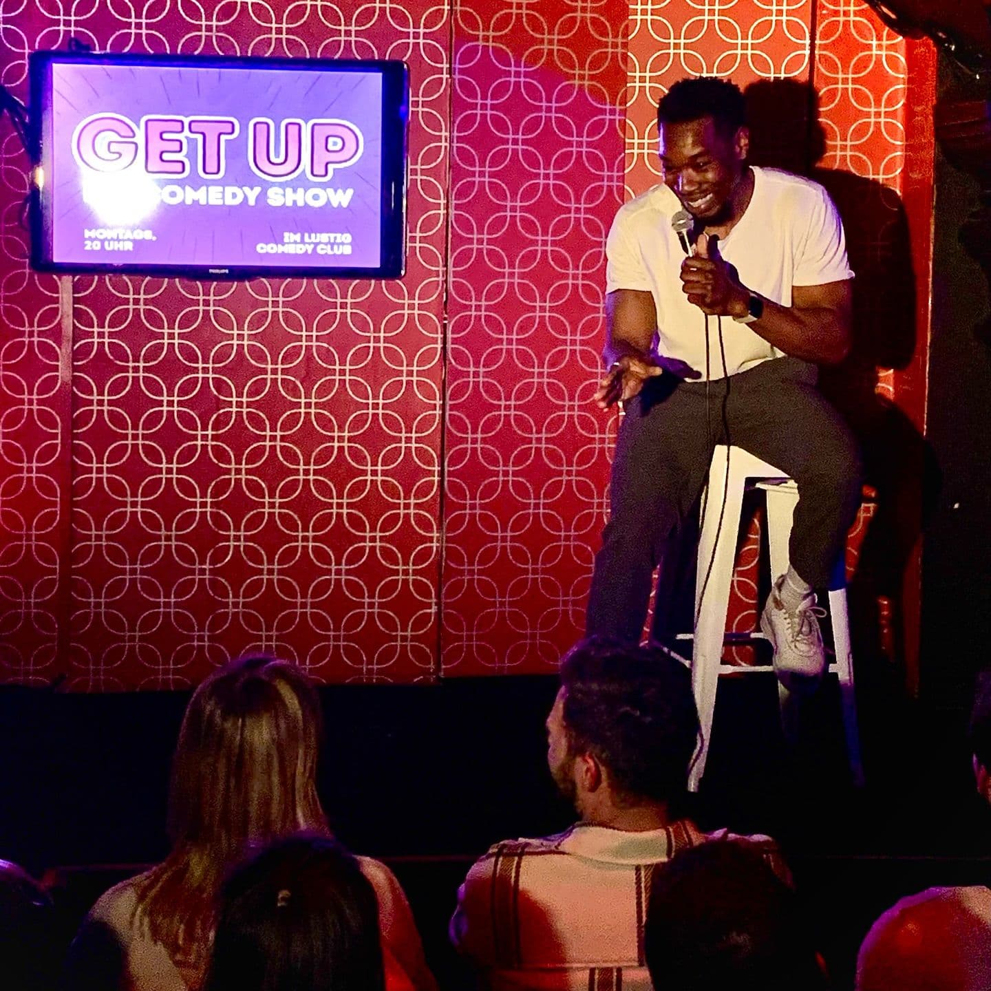 Ein Comedian sitzt mit einem Mikrofon lachend auf einer Bühne