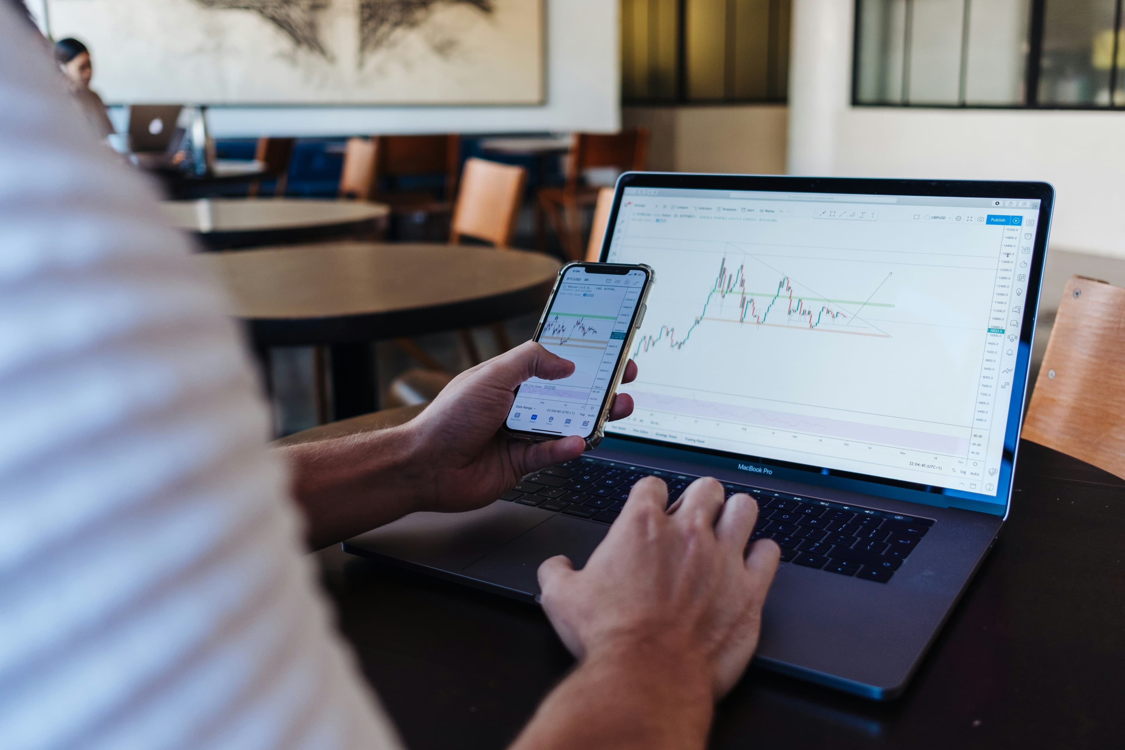 Eine Person hält ein Smartphone in der Hand und tippt mit der anderen auf einem Laptop