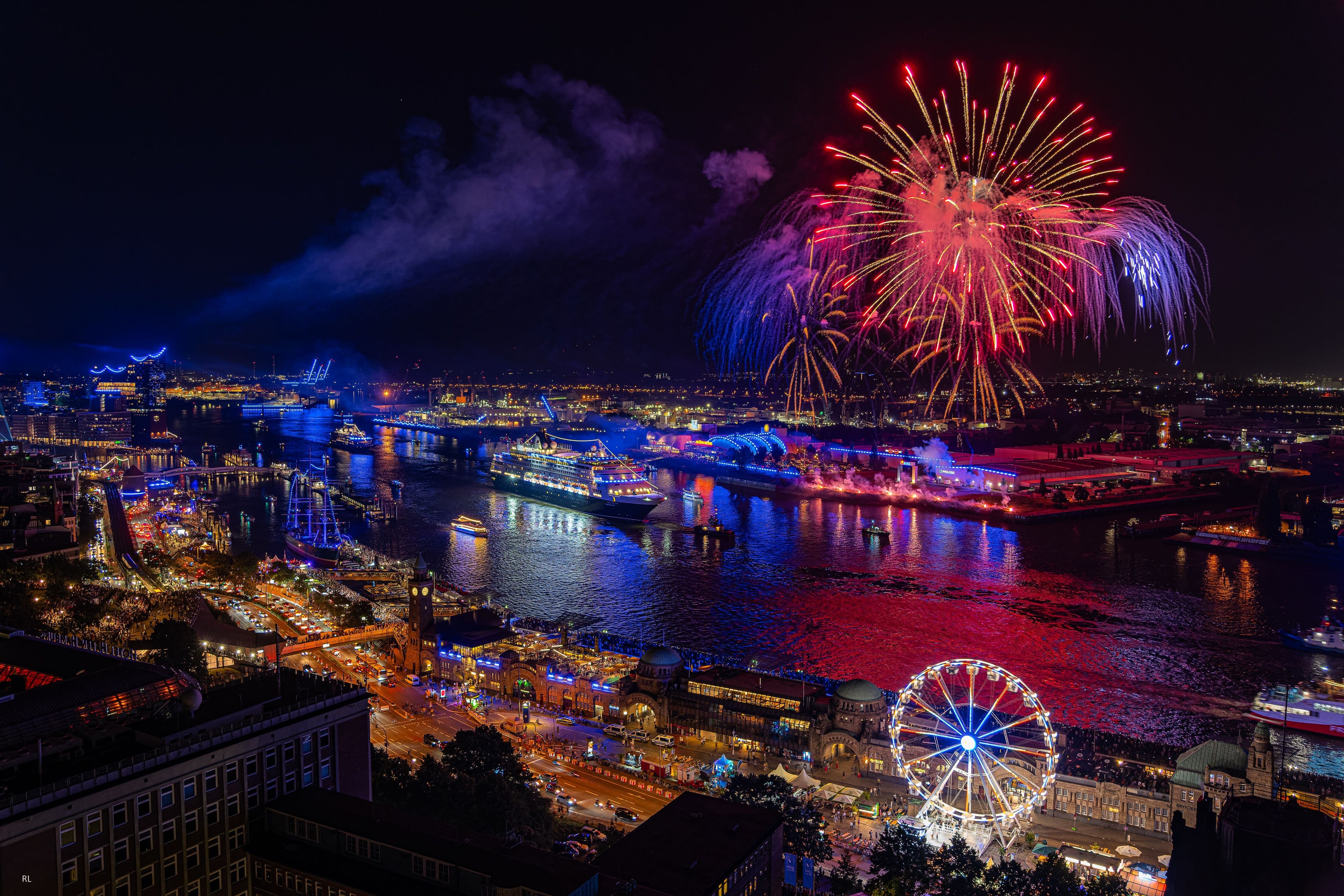 Sicht auf den Hamburger Hafen am Abend mit Kreuzfahrtschiffen und einem Feuerwerk über der Elbe