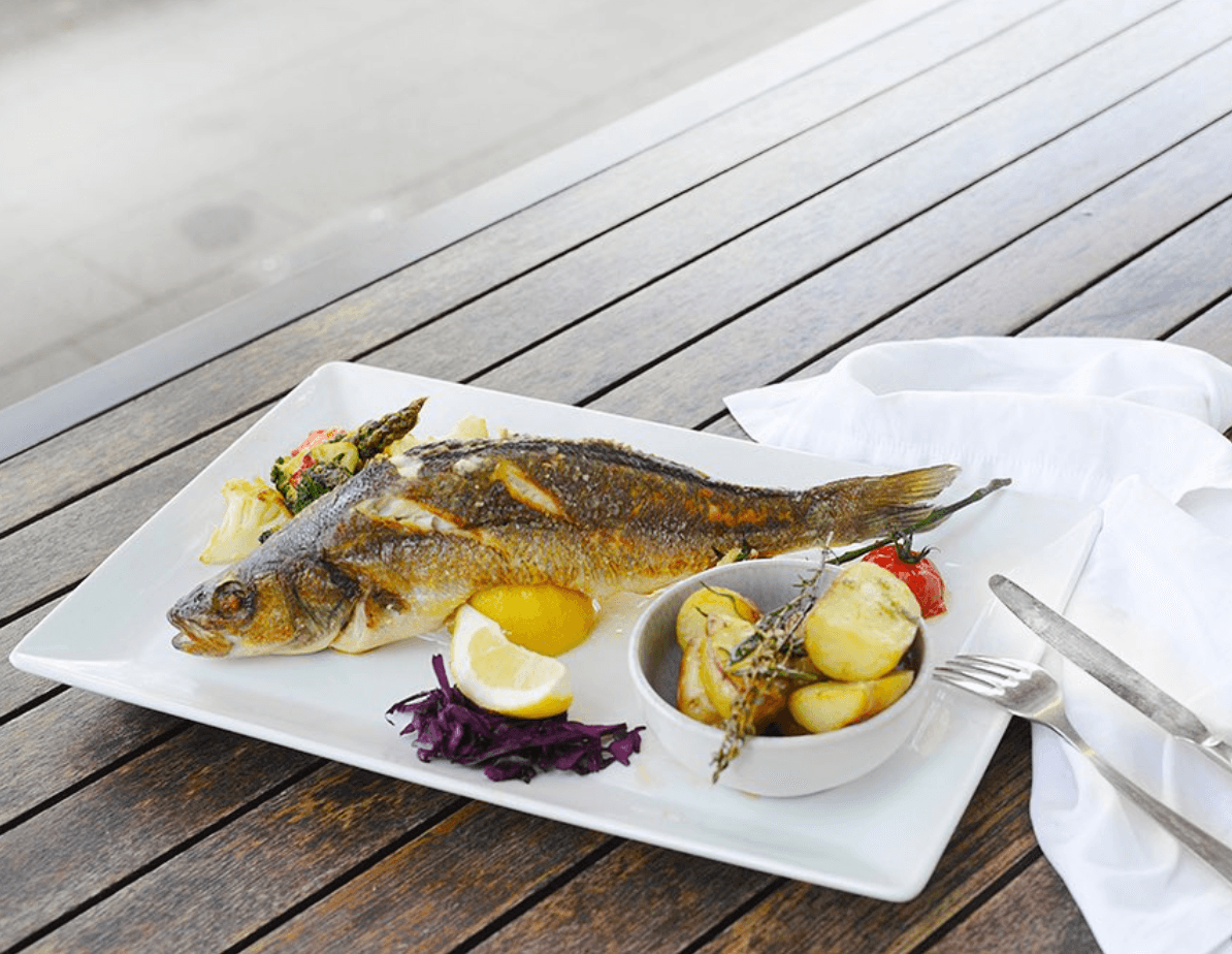 Ein ganzer Fisch liegt mit Kartoffeln und Salatbeilage auf einem weißen Teller