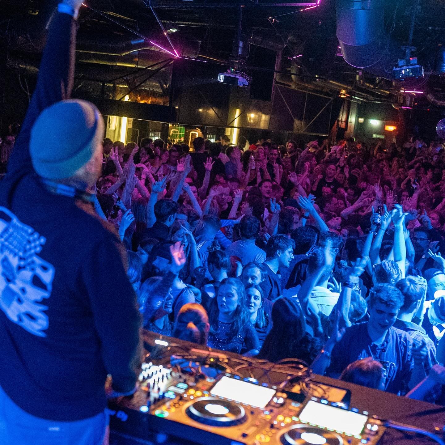 Ein DJ von hinten fotografiert. Vor ihm steht sein Publikum und feiert.