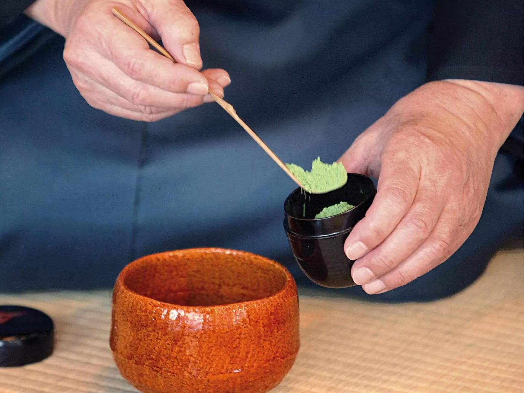 Eine Person löffelt Matcha-Pulver in ein Gefäß