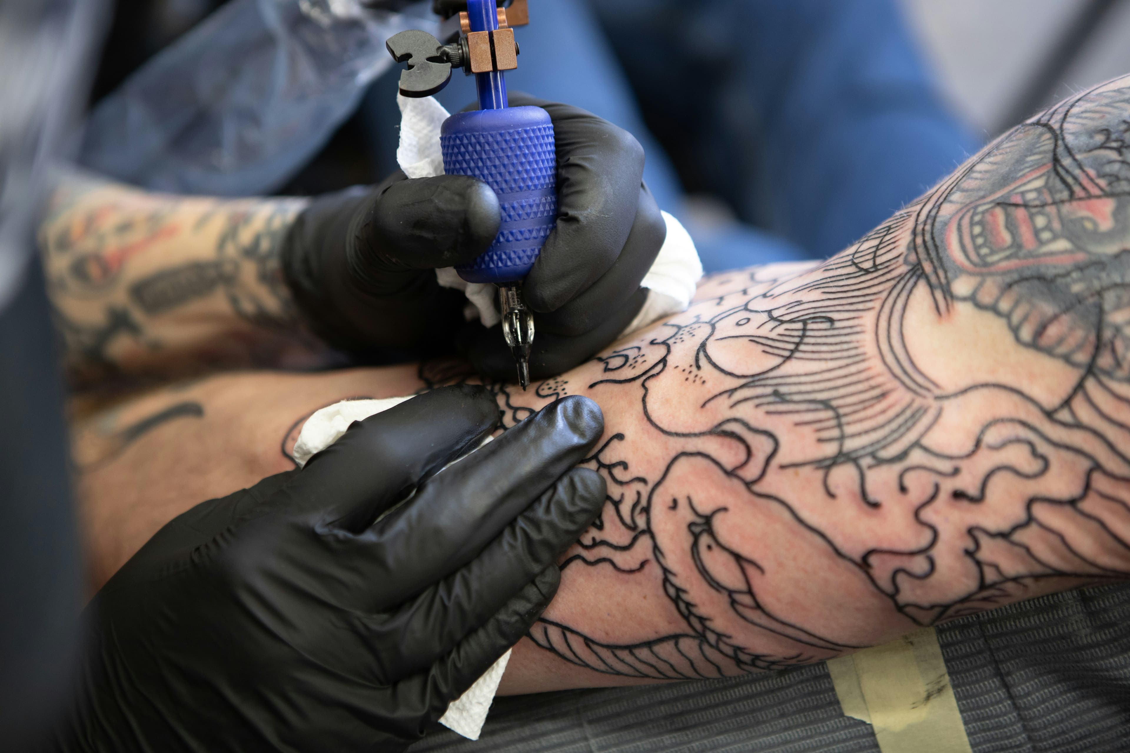Ein bereits tattowierter Arm, auf dem ein neues Tattoo gestochen wird