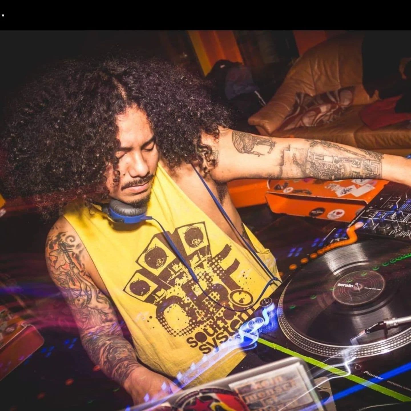 DJ mit langen, schwarzen Locken am DJ Pult