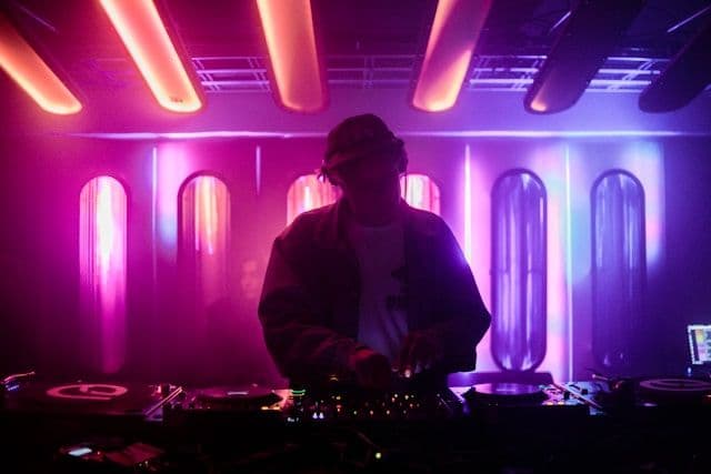 Ein DJ am Pult, hinter ihm pink bis violette Neon-Rähren