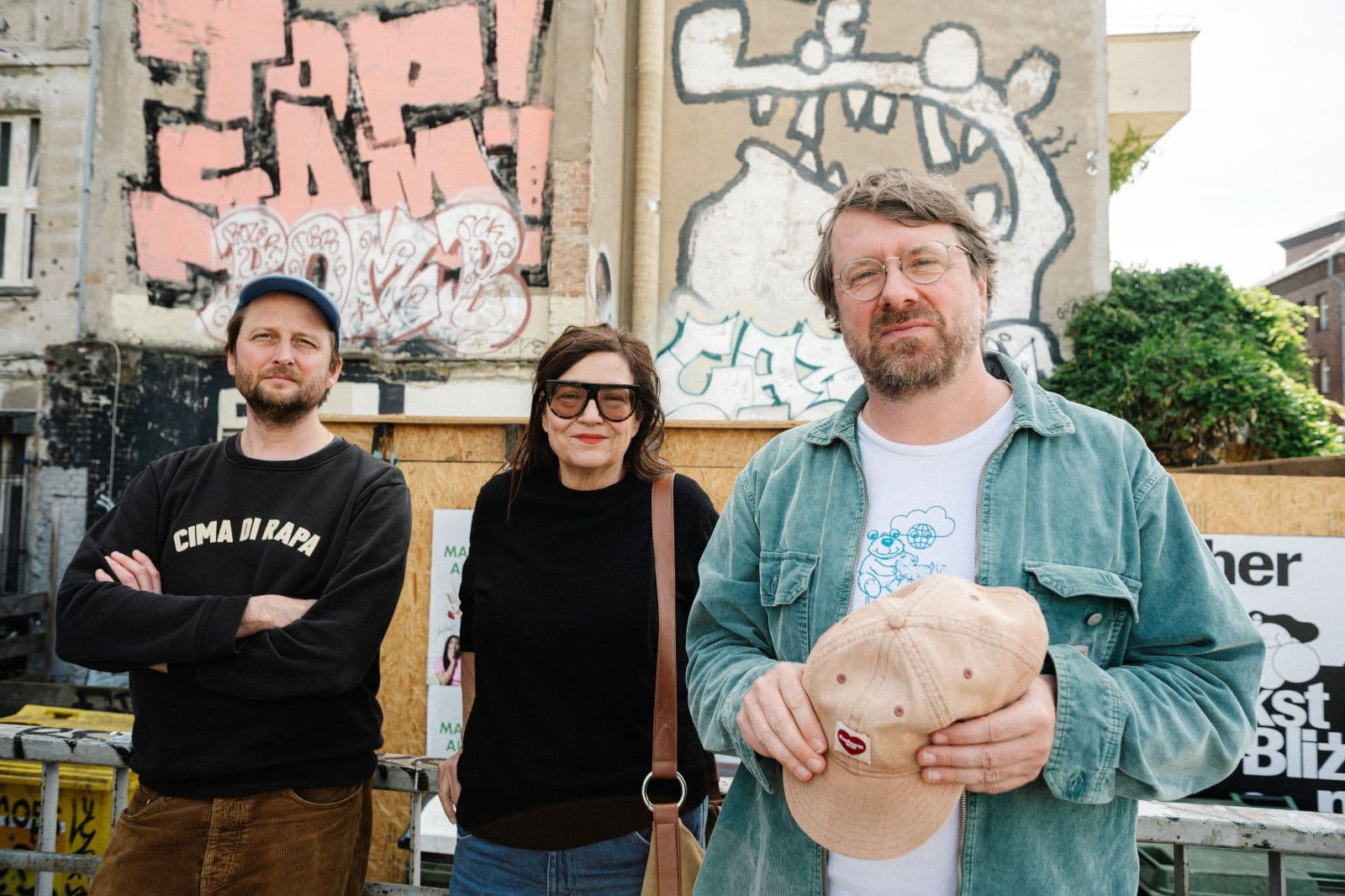 Die drei Mitglieder der CRUCCHI GANG stehen vor einer mit Graffiti besprühten Hauswand