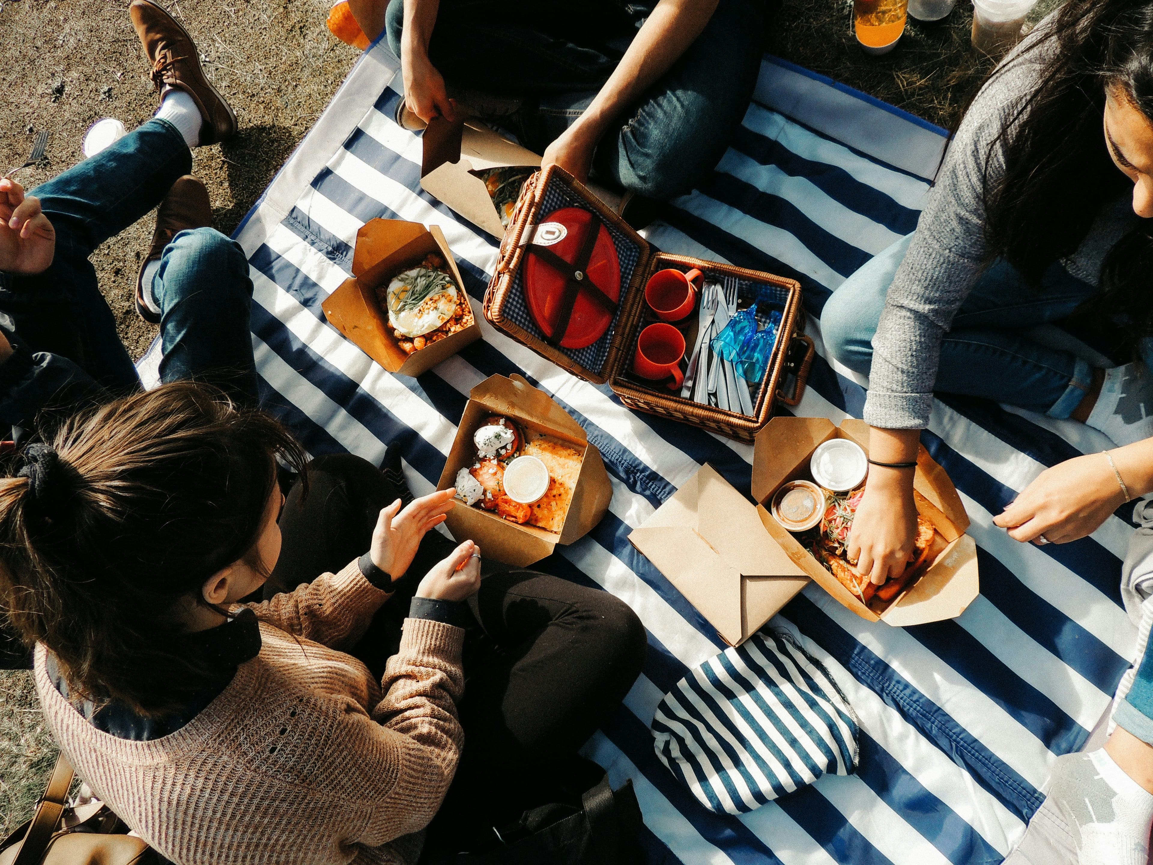 Vier Menschen sitzen auf einer gesteiften Decke und essen