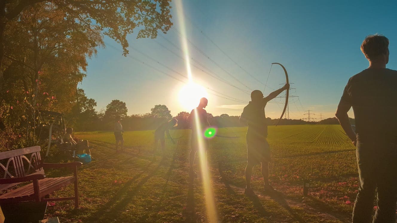 Personen schießen Pfeile im Sonnenuntergang