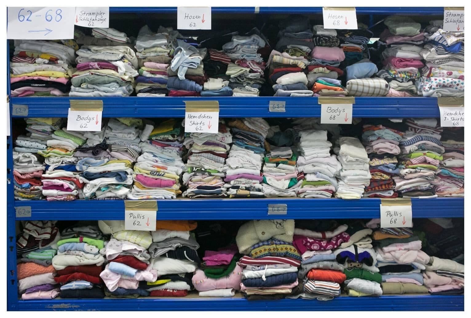 Kleiderspenden liegen sortiert in Regalen