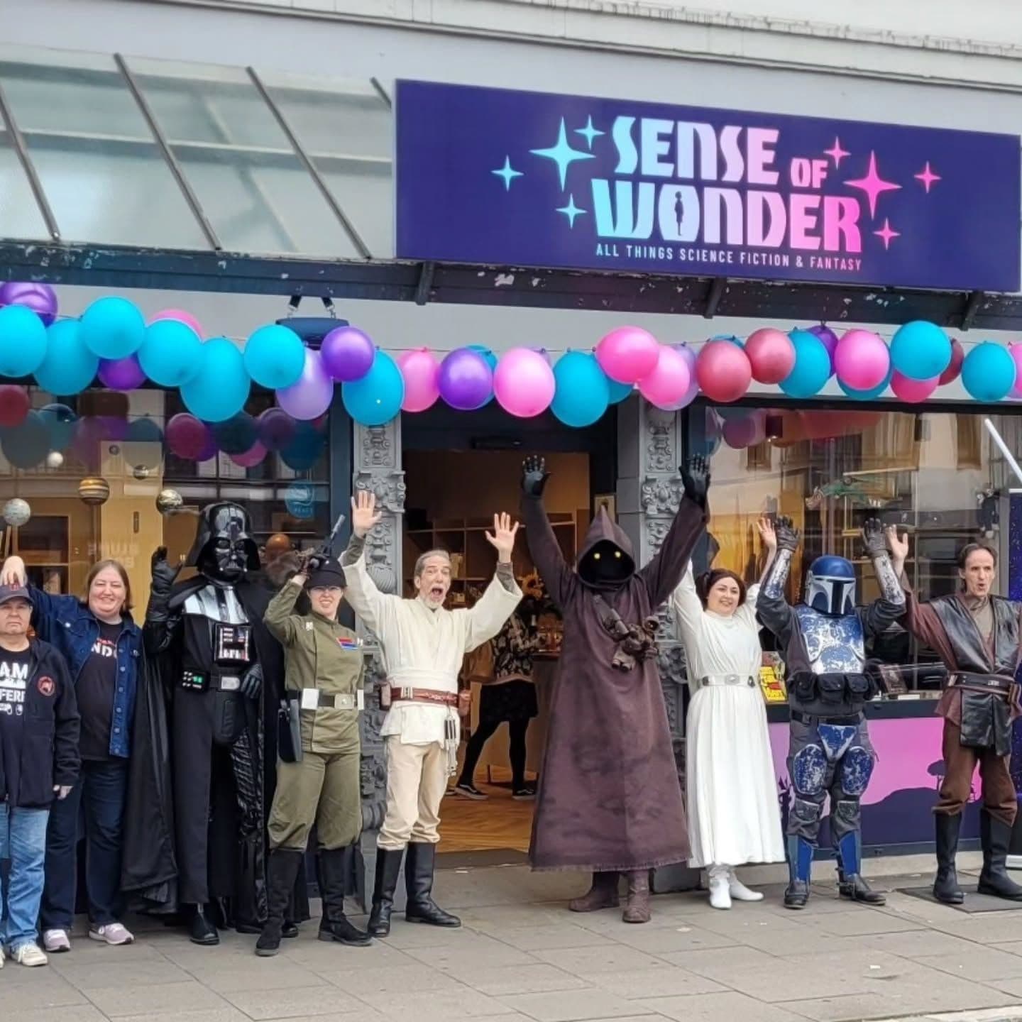 Verkleidete Menschen stehen vor dem mit bunten Ballons geschmückten Buchladen "Sense of Wonder"