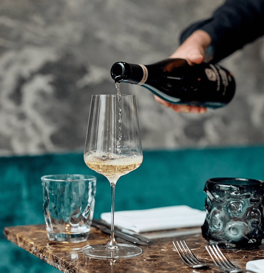 Person schenkt Schaumwein in ein Weinglas auf einem Marmortisch