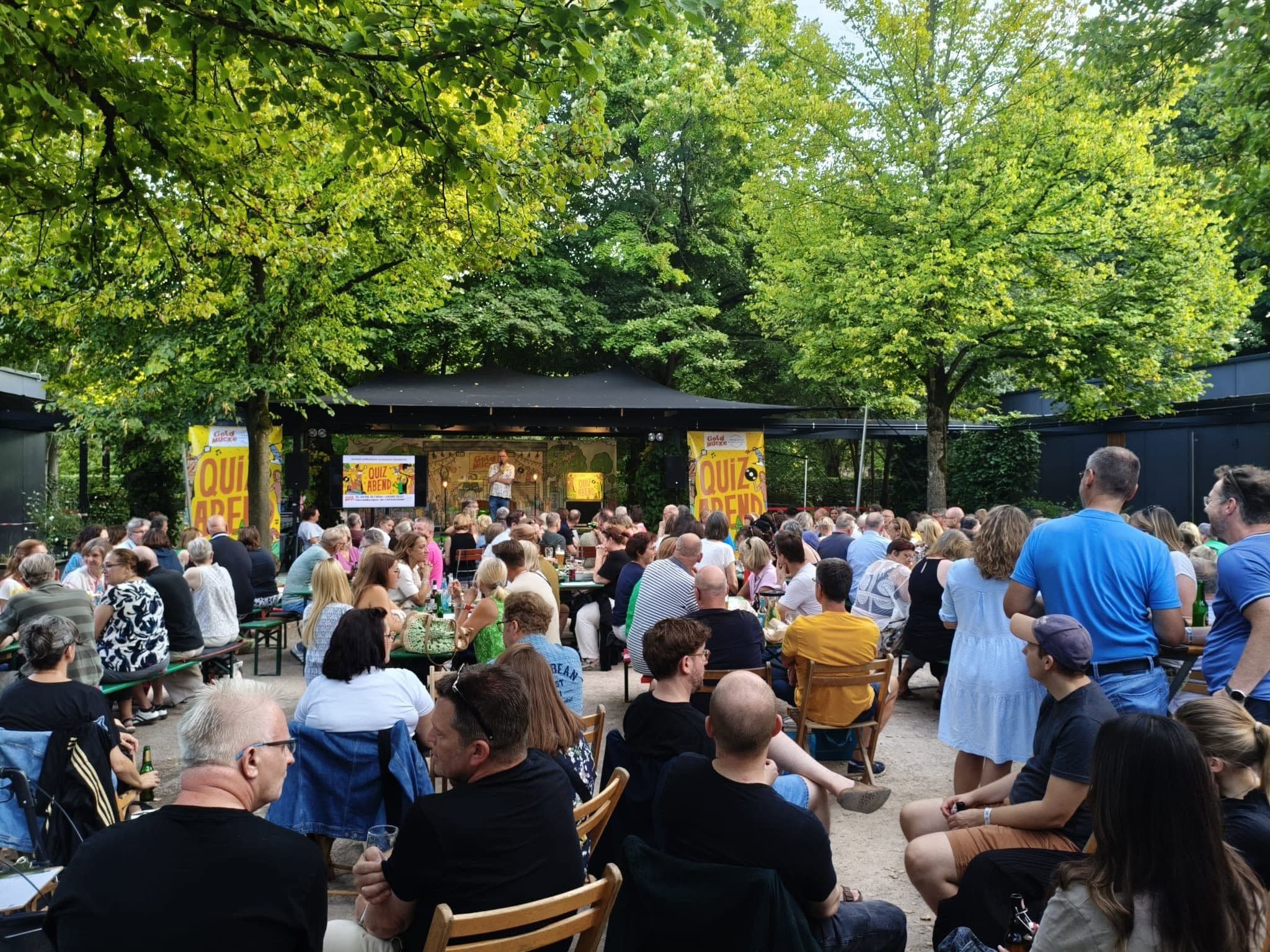 Menschen sitzen in einem Biergarten vor einer Bühne