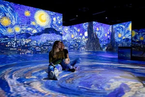 Zwei Besucherinnen sitzen in einer Installation von van Goghs Sternennacht