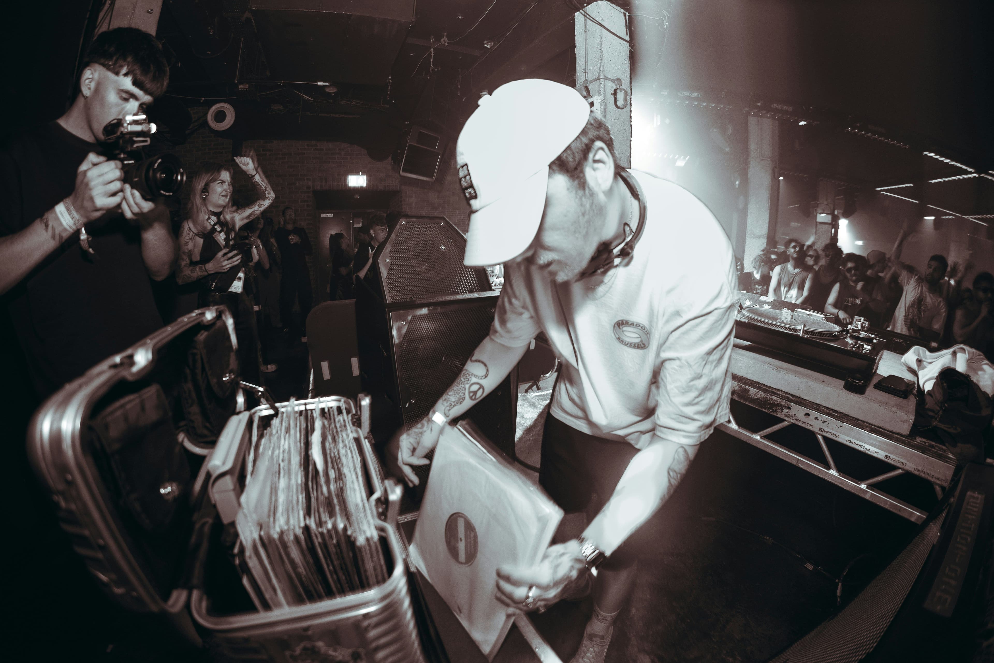 Ein DJ sucht nach einer Schallplatte und Menschen feiern im Hintergrund