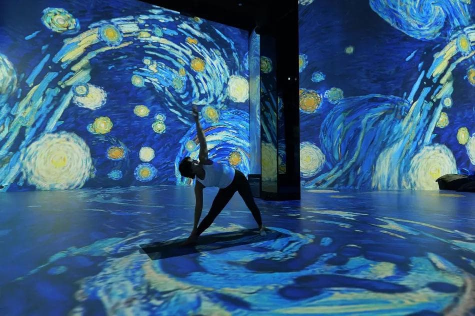 Eine Person macht Yoga umgeben von einer Projektion von Van Goghs Sternennacht