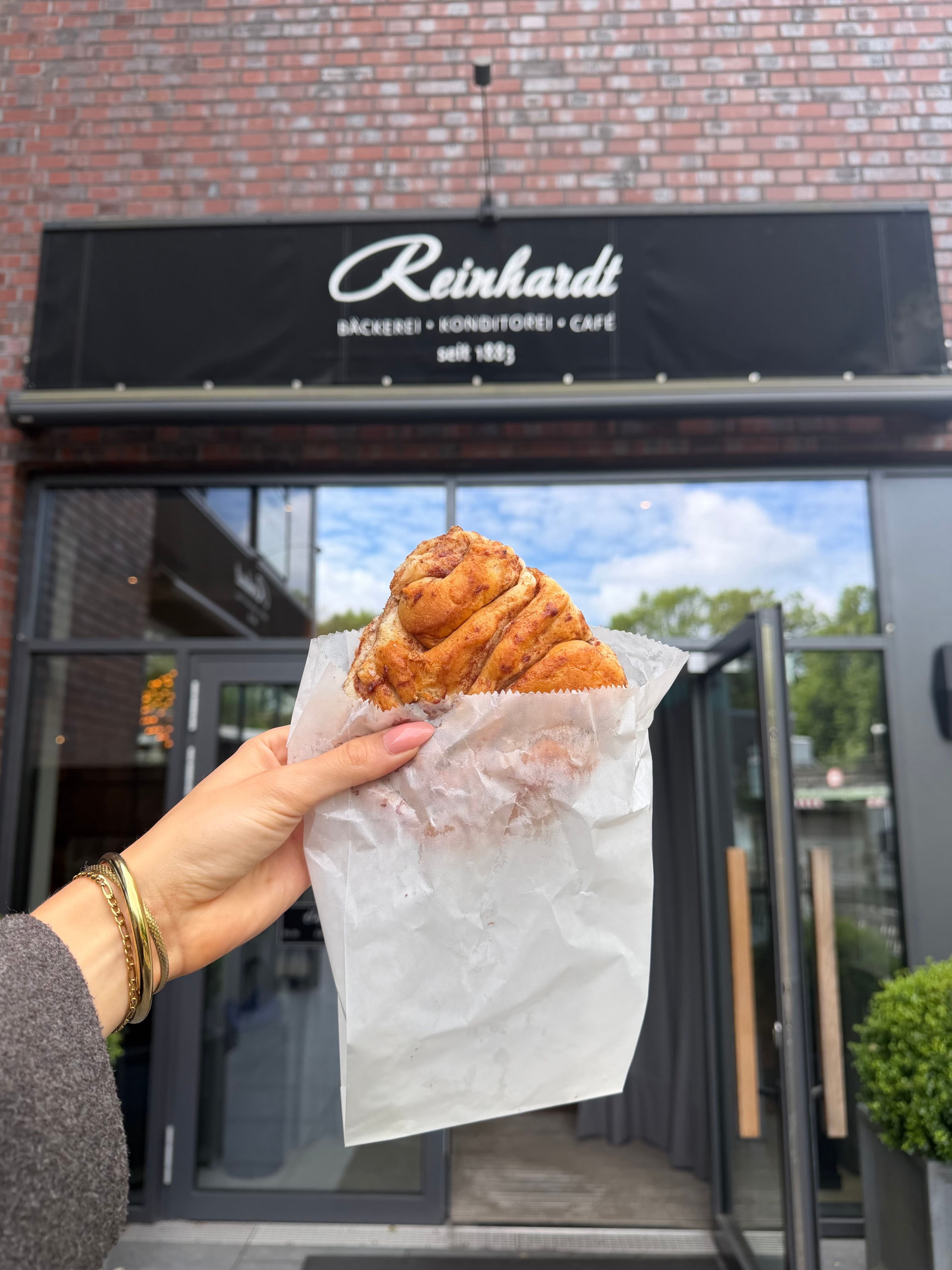 Ein Franzbrötchen in einer Hand vor dem Café Reinhardt