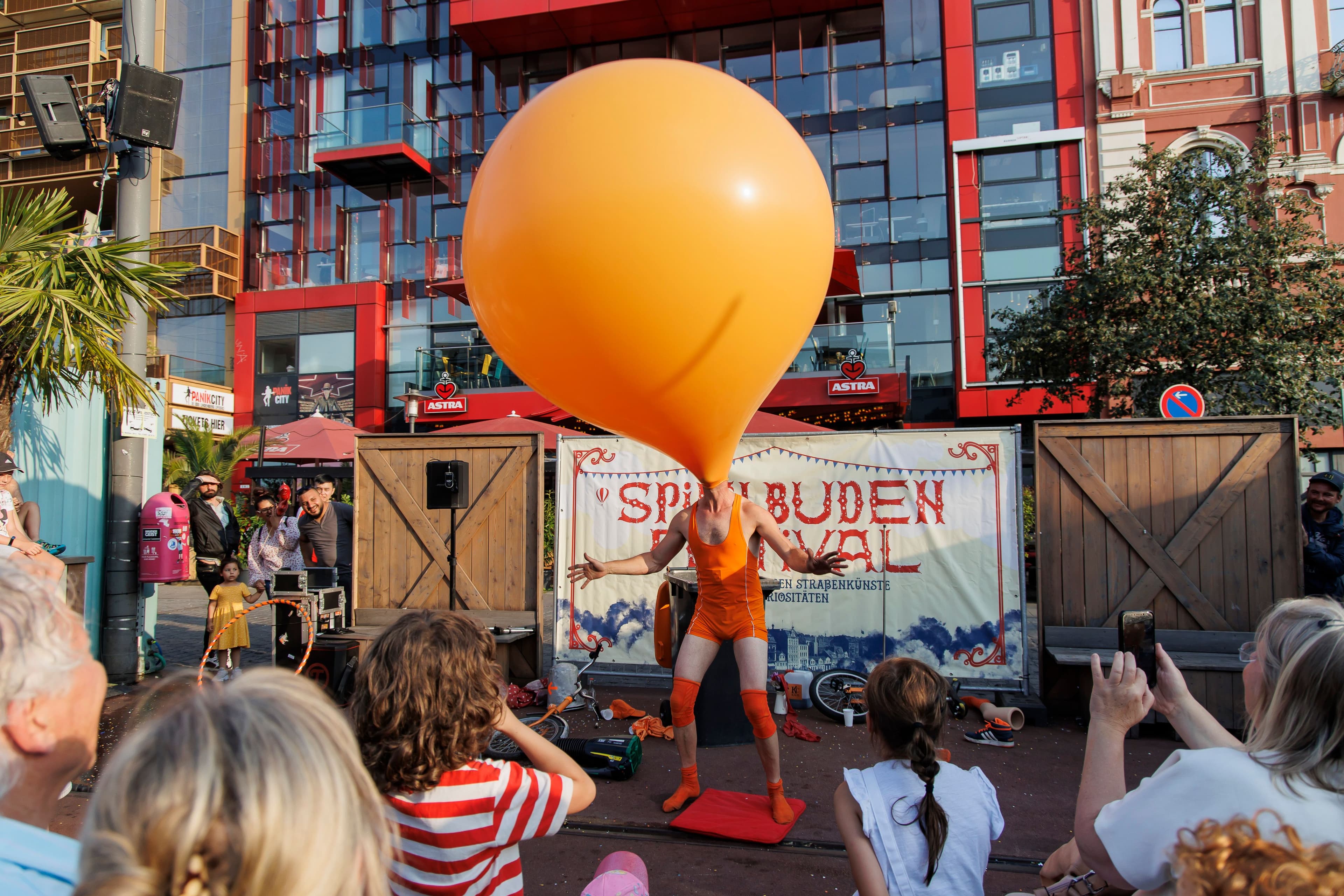 Kleinkünstler steht mit Ballon auf dem Kopf vor Publikum