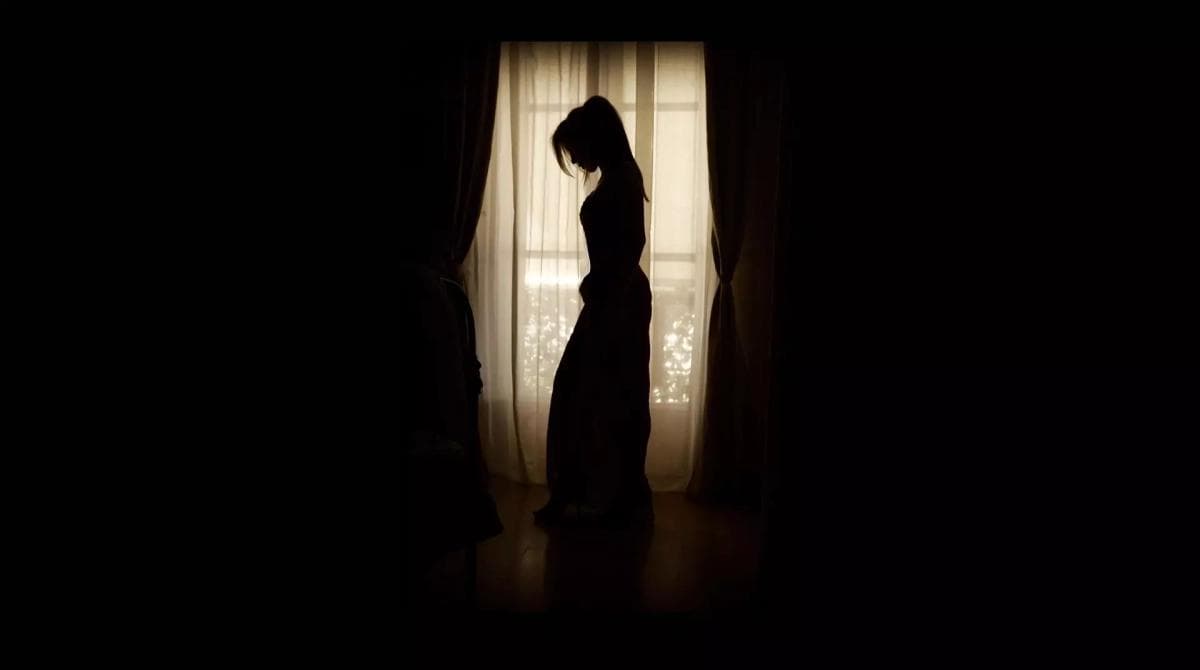 Eine Frau steht in einem dunklem Raum vor einem lichtdurchfluteten Fenster