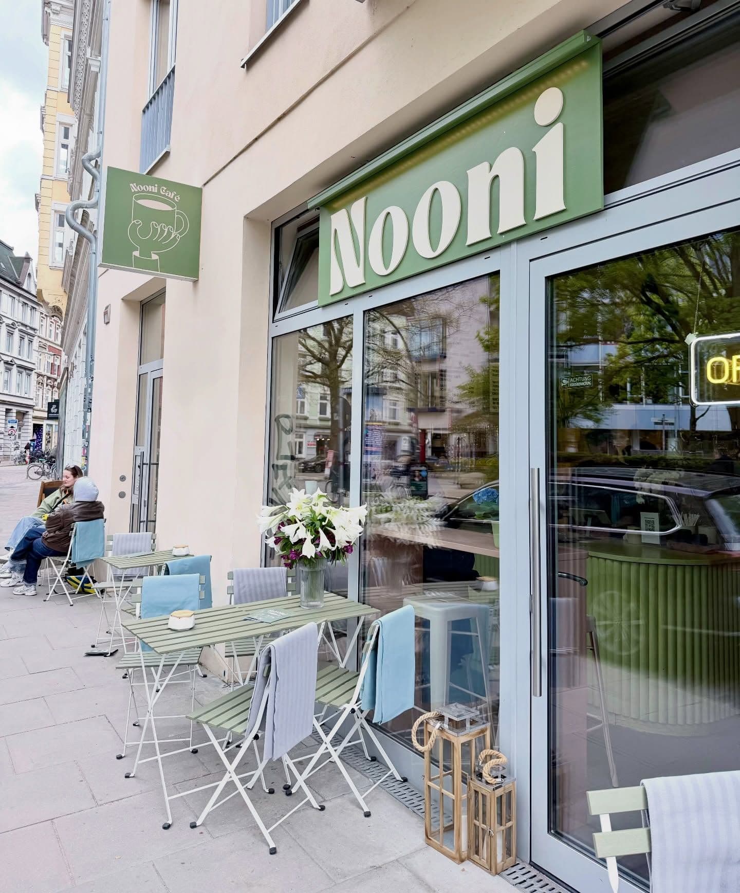 Außenansicht des Café Nooni mit Tischen und Stühlen davor