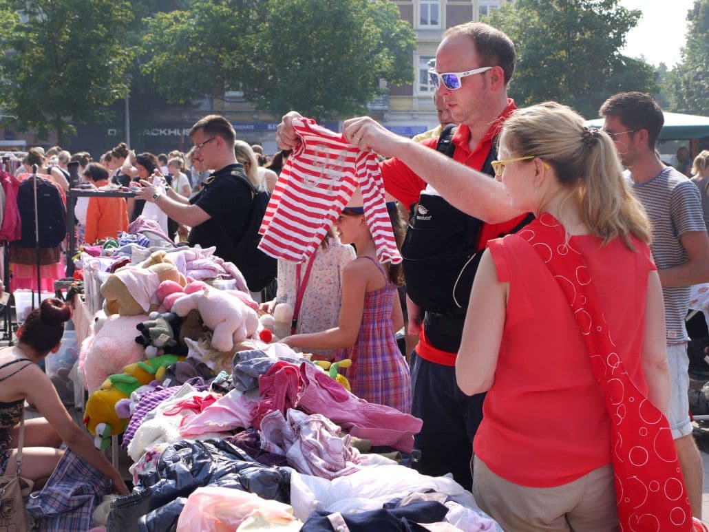 Eine Familie schaut sich einen Baby-Body an einem Flohmarkt-Stand an.